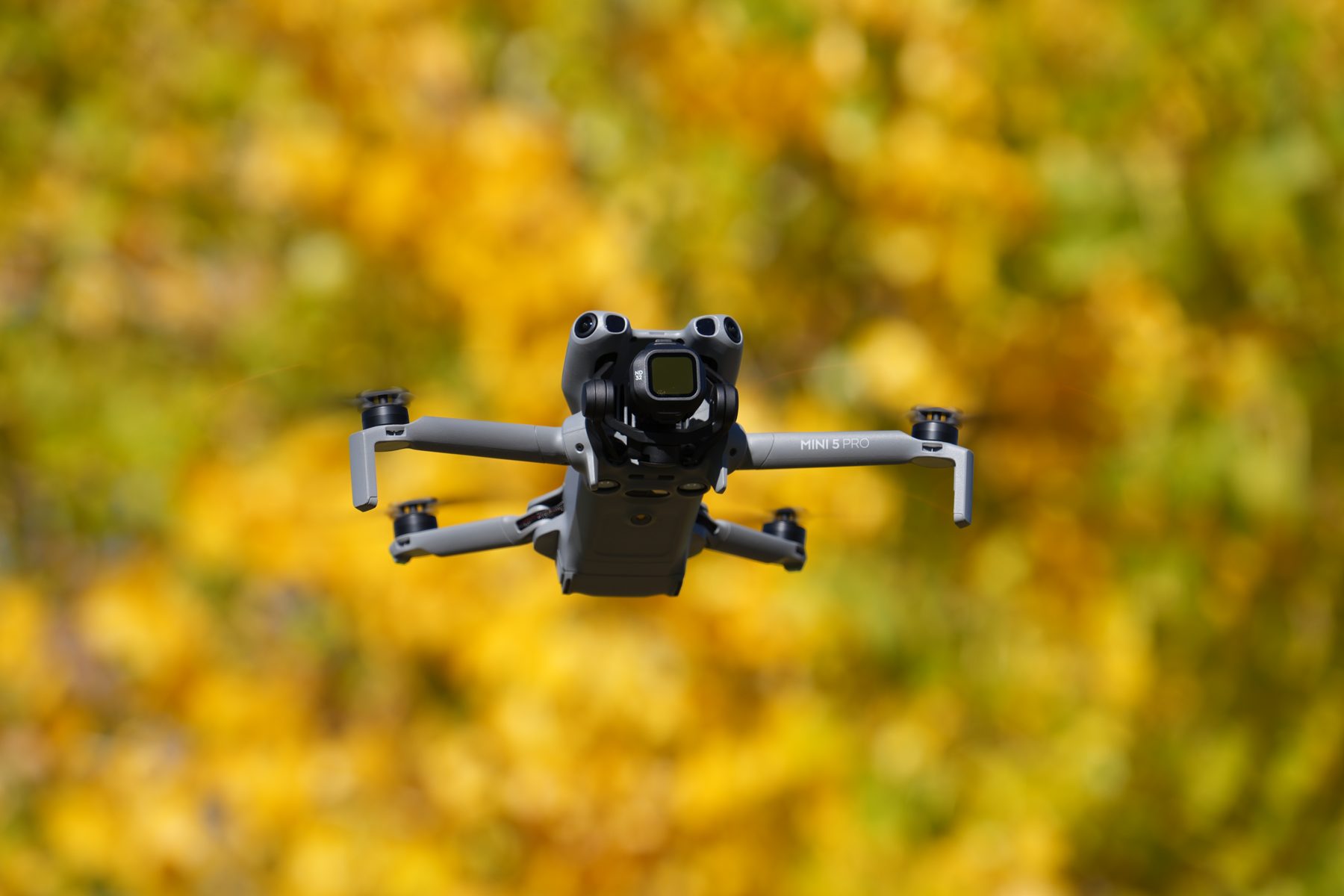 DJI Mini 5 Pro flying in front of fall foliage