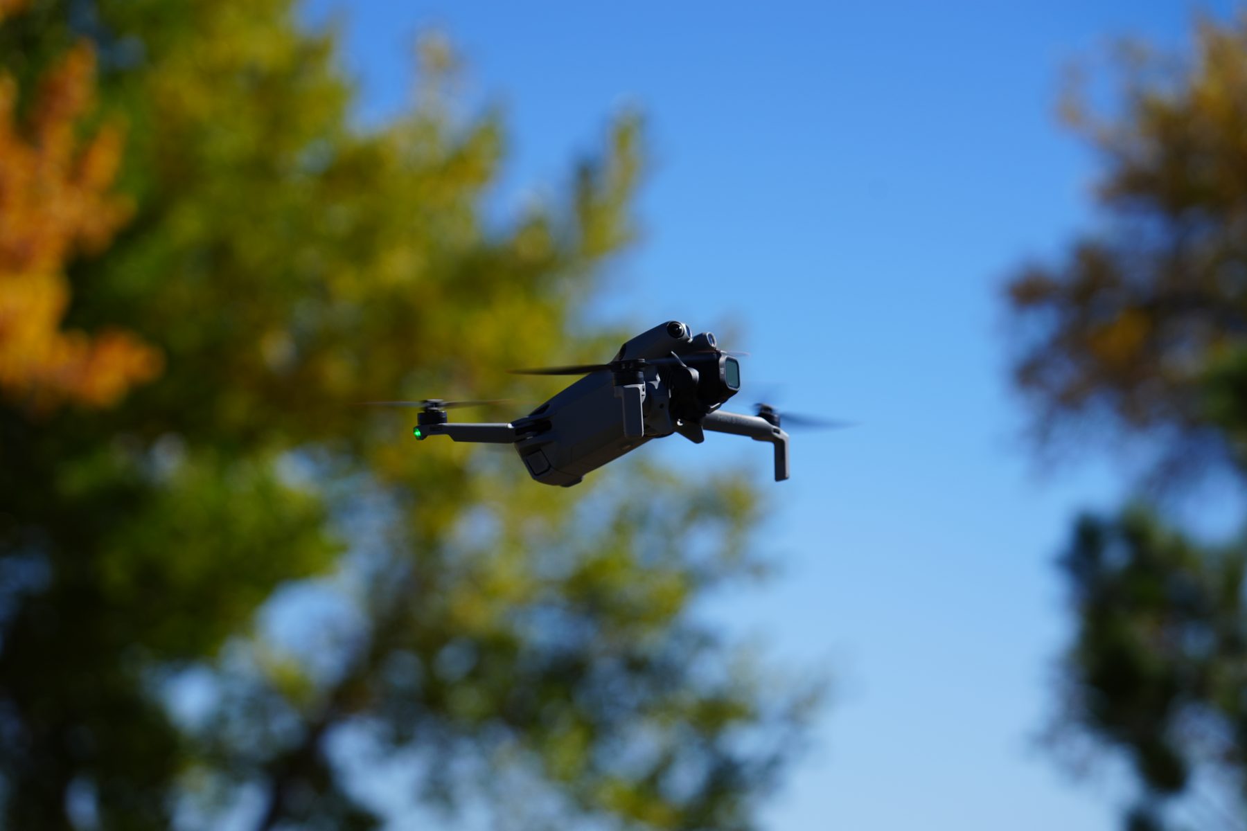 DJI Mini 5 Pro in flight against blue sky and fall trees
