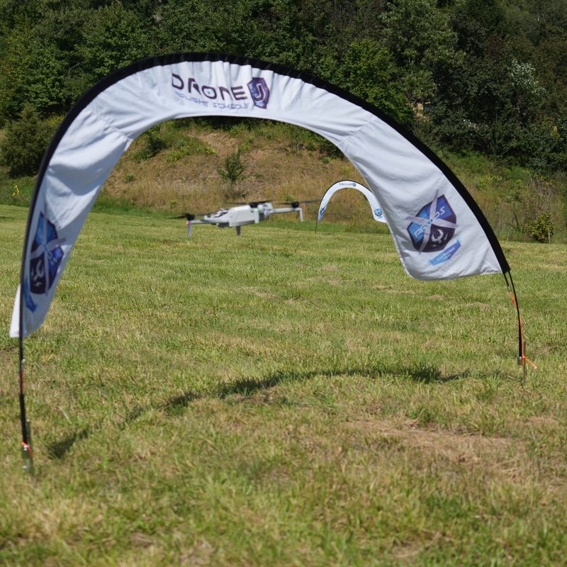Drone flying low toward a Drone U Flight School gate with more gates set up across the field behind it