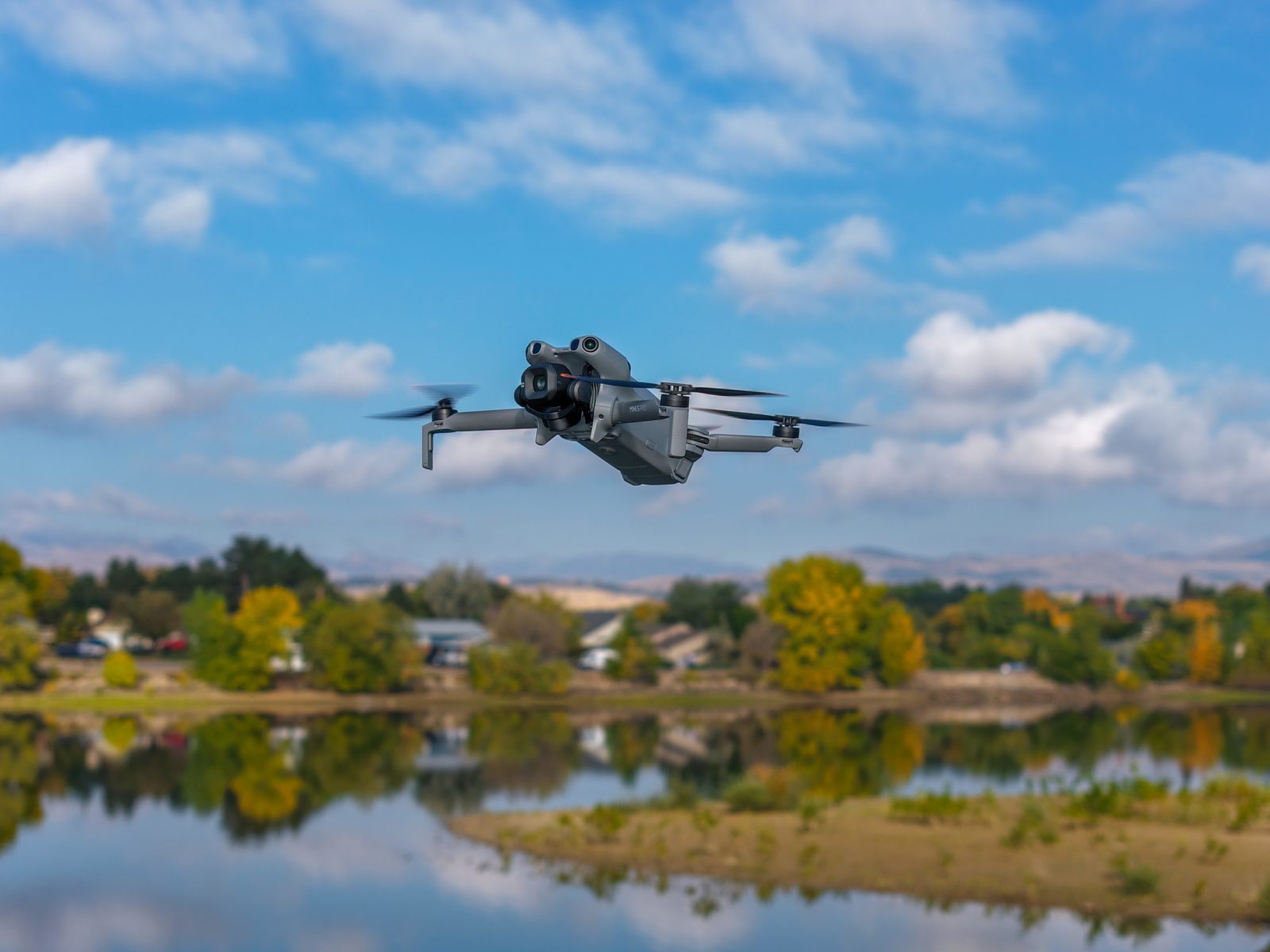 DJI Mini 5 Pro drone flying over a calm reflective lake lined with fall trees